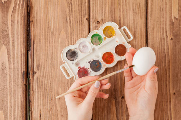 istock Close-up of woman's hands painting an easter egg on wooden background 1137972700
