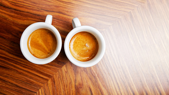 Two cups of espresso coffee on a wooden table.