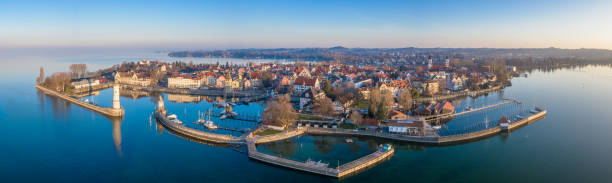 Lindau at Sunrise Aerial Panorama Bodensee Germany Aerial Drone Panorama at sunrise towards the Lindau Island, Old Town and Waterfront Cityscape. Lindau Harbor Bodensee Entrance with the famous old Lighthouse (left) and Bavarian Lion Sculpture from the year 1856. Lindau Waterfront Promenade with Mangenturm, Restaurants and Hotels in the Background. Stiched XXXL Panorama. Lindau, Bodensee, Bavaria, Germany. lindau lighthouse stock pictures, royalty-free photos & images