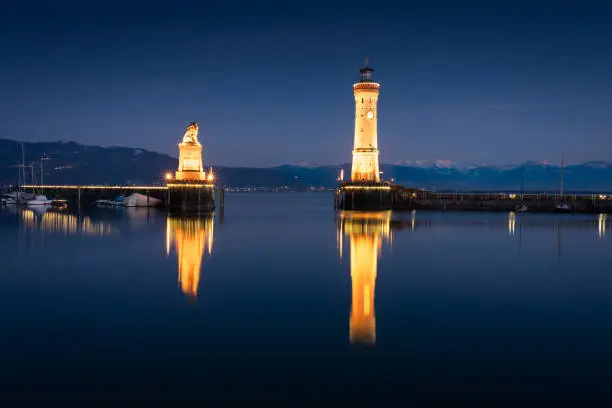Illuminated Harbour Entrance of Lindau with Lighthouse and Bavarian Lion Sculpture from the year 1856 illuminated at Night - Twilight. Lindau, Bodensee, Bavaria, Germany.
