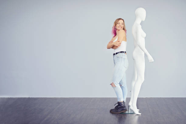 Studio shot of a young woman posing next to a mannequin against a grey background