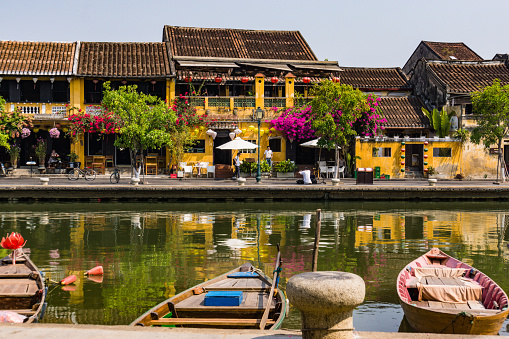 scene from the old historic town of Hoi An along the river with boats, lanterns, flowers and the gold yellow Hoi An buildings with tile roofs