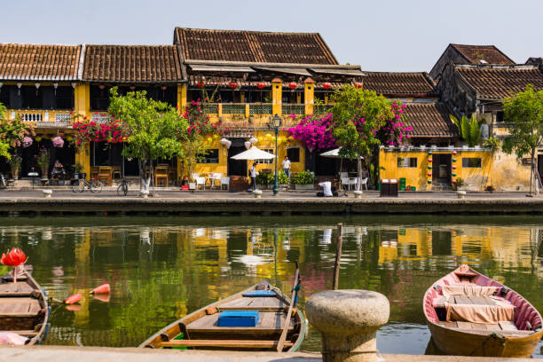 old Hoi An river scene scene from the old historic town of Hoi An along the river with boats, lanterns, flowers and the gold yellow Hoi An buildings with tile roofs hoi an stock pictures, royalty-free photos & images