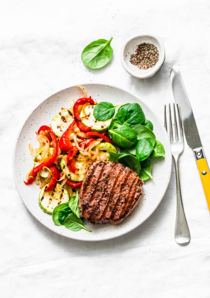 istock Beef steak with grilled  vegetables, sweet pepper, zucchini and fresh spinach on a light background, top view. Delicious healthy balanced lunch 1137980517
