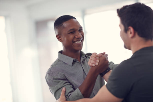 Sometimes business partners, sometimes bros Shot of two young businessmen gripping hands in solidarity in a modern office office buddies stock pictures, royalty-free photos & images