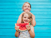 Two little sisters together with red ripe watermelon smiling. Over blue plank wall background