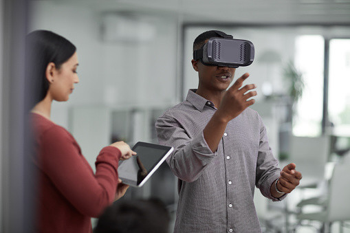 Shot of two young colleagues using a digital tablet and a virtual reality headset in a modern office