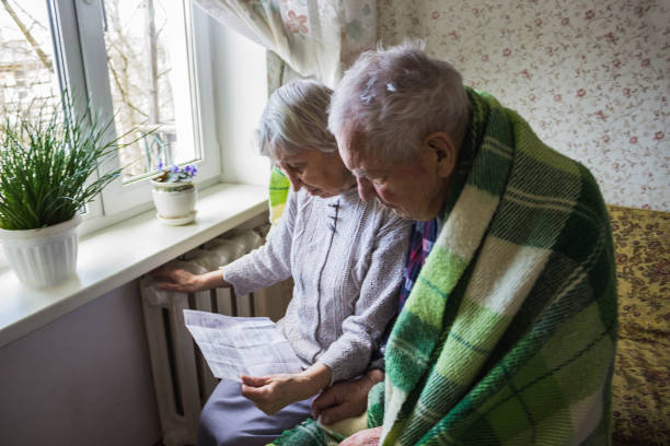 mujer sosteniendo efectivo delante del radiador calefactor. pago por calentamiento en invierno. enfoque selectivo. - women poverty senior adult mature adult fotografías e imágenes de stock