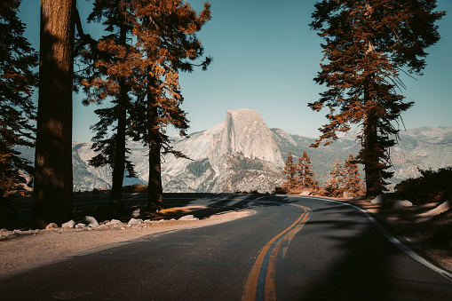 Beautiful view of winding Glacier Point Road with famous Half Dome summit in golden evening light at sunset, Yosemite National Park, California, USA