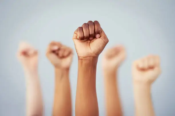 Cropped studio shot of a group of women raising their fists in solidarity against a gray background