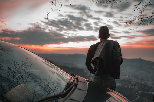 Man parked the car at sunset. Pointing  back and looking at the horizon