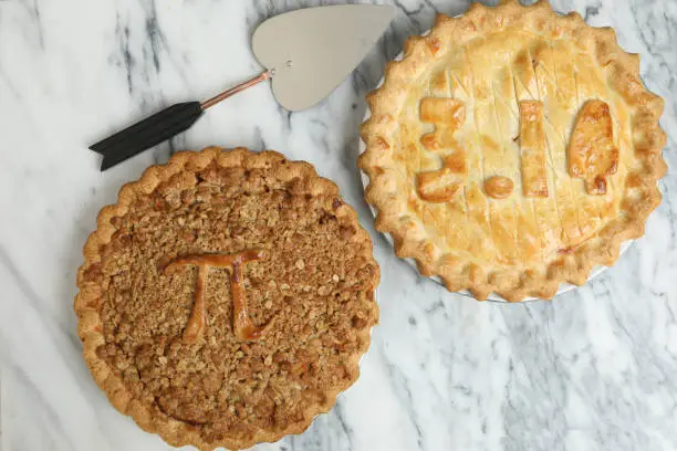 An overhead close up horizontal photograph of two Pi Pies, one displays the π symbol itself and the other one shows the value of 3.14. The pies were baked to commemorate March the 14th as Pi Day.