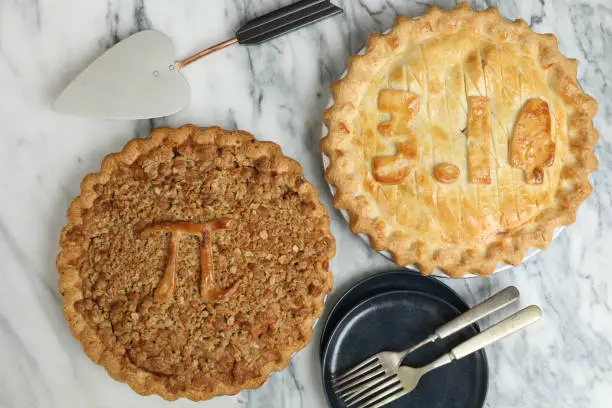 An overhead close up horizontal photograph of two Pi Pies, one displays the π symbol itself and the other one shows the value of 3.14. The pies were baked to commemorate March the 14th as Pi Day.