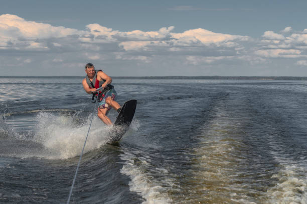 uomo teso wakeboard in un lago e trainato da una barca - wakeboarding nautical vessel wake jumping foto e immagini stock