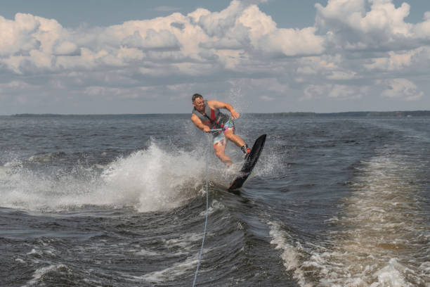 uomo teso wakeboard in un lago e trainato da una barca - wakeboarding nautical vessel wake jumping foto e immagini stock