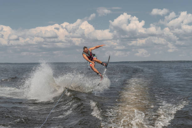 uomo teso che si sveglia in un lago e trascinato da una barca. saltare dall'onda - wakeboarding nautical vessel wake jumping foto e immagini stock