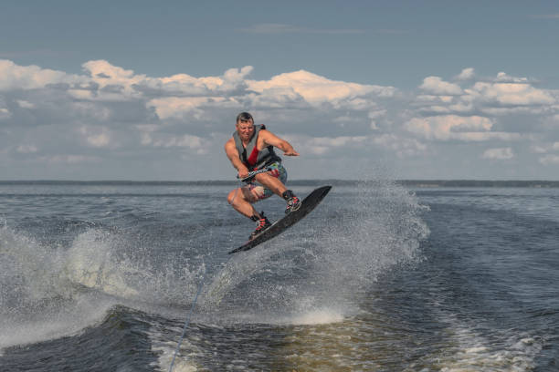 uomo teso che si sveglia in un lago e trascinato da una barca. saltare dall'onda - wakeboarding nautical vessel wake jumping foto e immagini stock