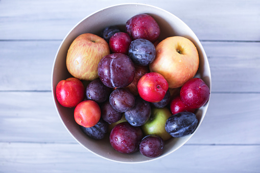 Plum and apples in bowl on a wooden table top view. Beautiful fresh fruits.