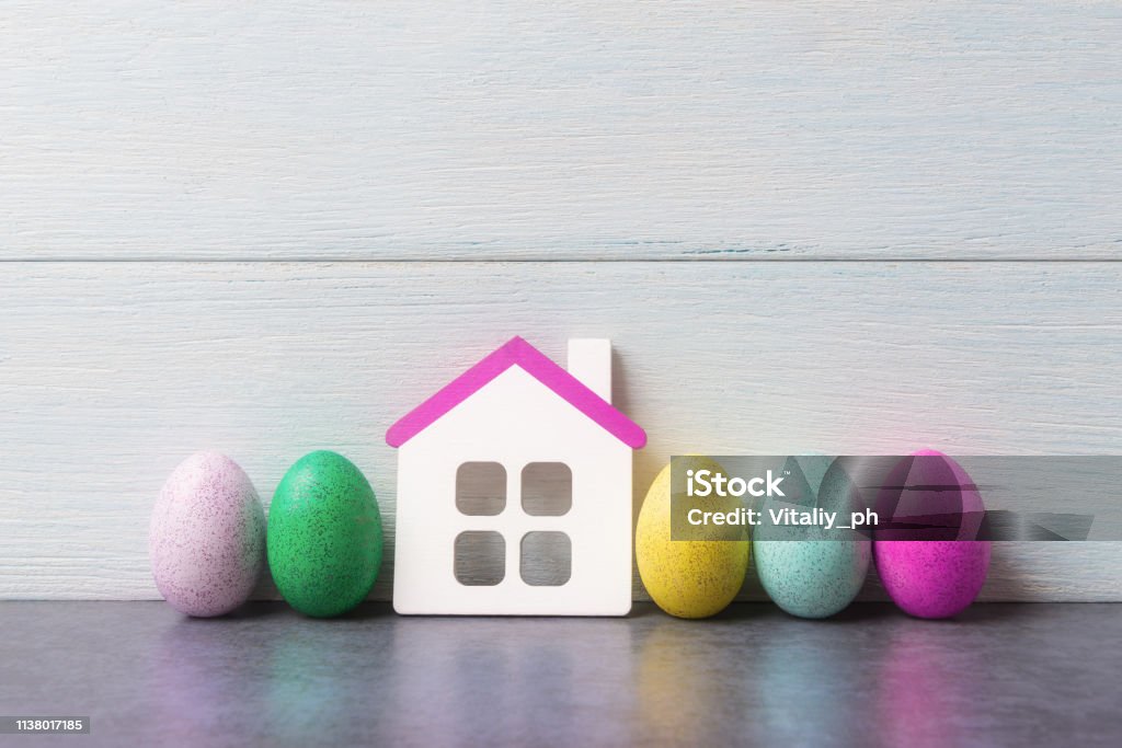 House model and painted Easter eggs over white wooden background. House Stock Photo