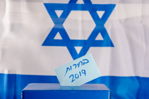 istock Vote box. Hebrew text Elections 2019 on voting paper over Israel flag background. 1138021435