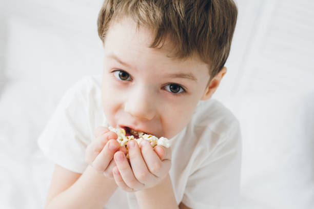 istock Cute boy eating popcorn sitting in bed with white linens 1138021695