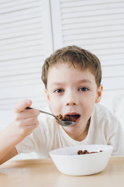 istock Cute boy eating Breakfast chocolate balls sitting in bed with white linens 1138022339