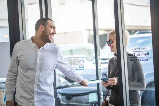 Photo of Store Owner Opens Door for Customer at Local Coffee Shop