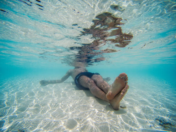 istock underwater picture of a young man lying down on the beach shore. Clear blue water 1138024162