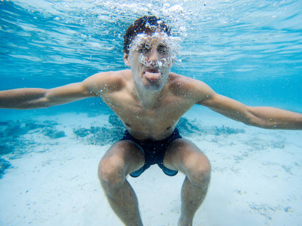młody człowiek co grymasy pod wodą. czysta niebieska woda. - underwater mine zdjęcia i obrazy z banku zdjęć