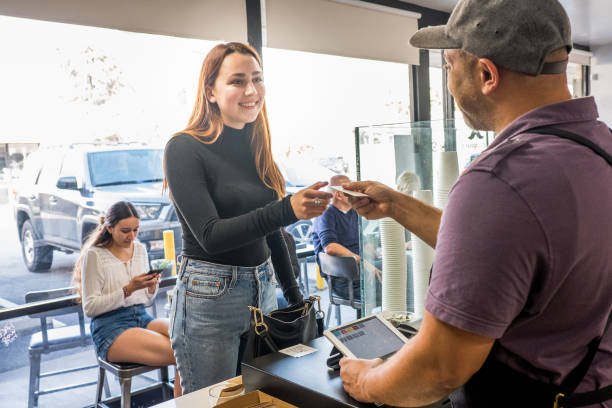 Teenage Female Customer Buying Coffee at a Coffee Shop Teenage girl paying for her coffee at the register. The employee hands her credit card back to her. point of sale tablet stock pictures, royalty-free photos & images