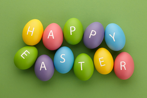 Colorful painted eggs with letters arranged in Happy Easter greeting on green background. Holiday concept.