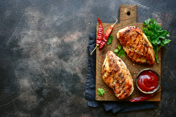 Grilled spicy chicken breast with ketchup Grilled spicy chicken breast with ketchup on a wooden cutting board over dark slate, stone, concrete or metal background.Top view with copy space. chicken breast photos stock pictures, royalty-free photos & images