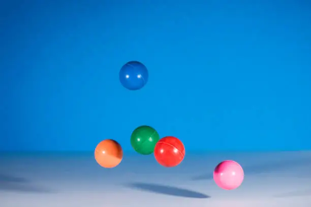 5 multicolor rubber balls in mid air against a blue background