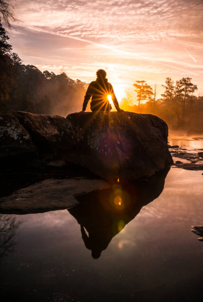 Sunrise in front of person sitting on rock.