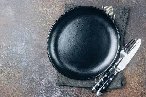istock Black plate, cutlery and napkin on stone table top view 1138052685