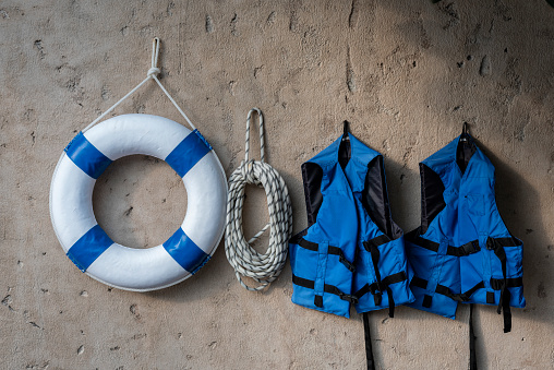 Life buoy hanging, blue life jacket and rope on concrete wall for emergency response when people sinking to water almost place near pool and beach