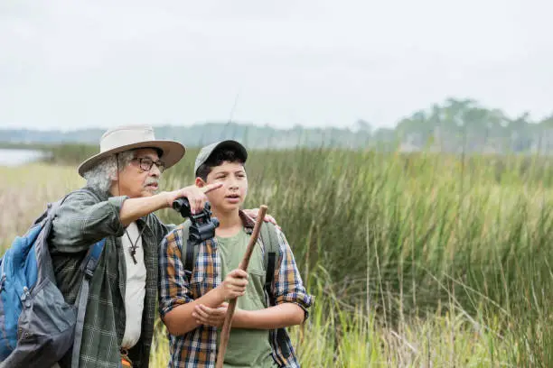 Photo of Hispanic boy hiking with grandfather, bird watching