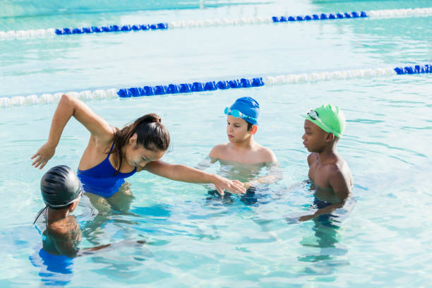 Young woman giving swim lessons to multi-ethnic group A young woman, 19 years old, Chinese ethnicity, standing in a swimming pool with a multi-ethnic group of boy, giving them a swimming lesson on freestyle. The children are 9 and 10 years old. swimming stock pictures, royalty-free photos & images