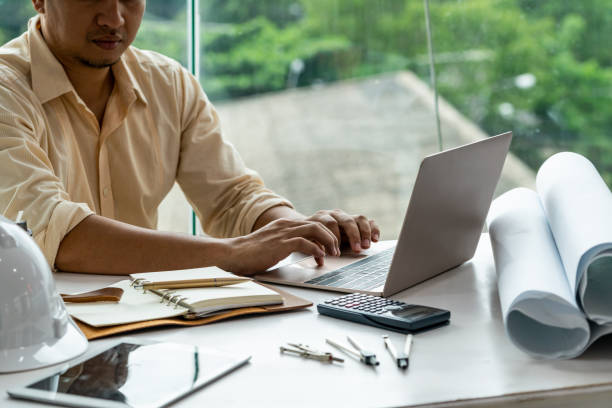 istock Young man architect or engineer working at desk with designer equipment to make interior design at workplace. Real estate business and civil engineering concept. 1138081824
