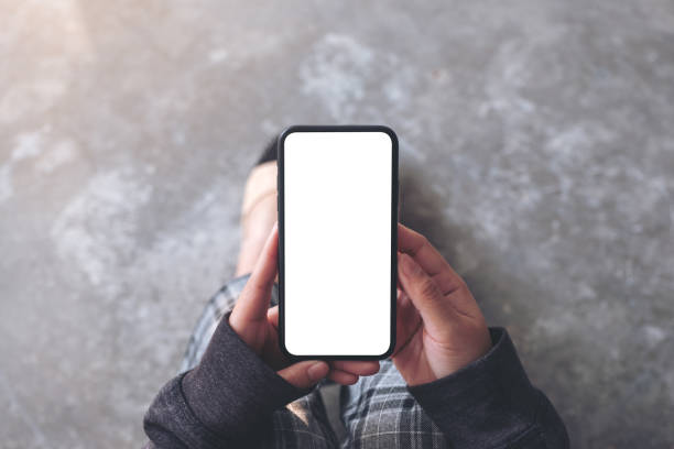 a woman holding black mobile phone with blank desktop screen while sitting on the floor - full screen imagens e fotografias de stock