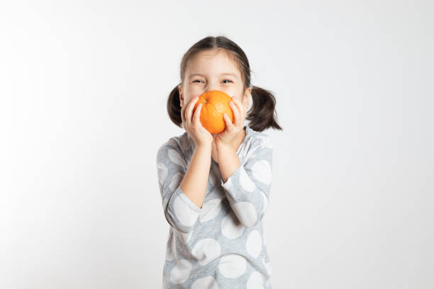 Girl Holding Orange Girl is holding an orange in front of her face. preschooler caucasian one person part of stock pictures, royalty-free photos & images