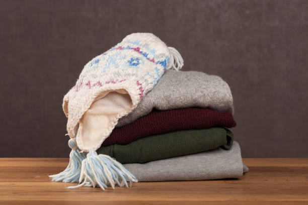 istock Bunch of knitted warm pastel color sweaters with different knitting patterns folded in stack on brown wooden table, grunged texture wall background 1138099096