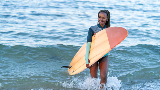 Afro Surfer girl walking out the sea and carrying surfboard