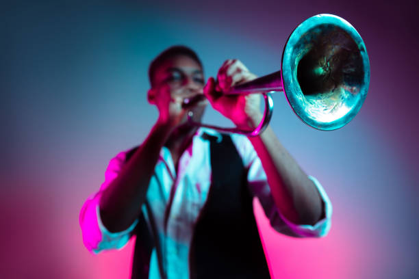 African American jazz musician playing trumpet. African American handsome jazz musician playing trumpet in the studio on a neon background. Music concept. Young joyful attractive guy improvising. Close-up retro portrait. trumpet stock pictures, royalty-free photos & images