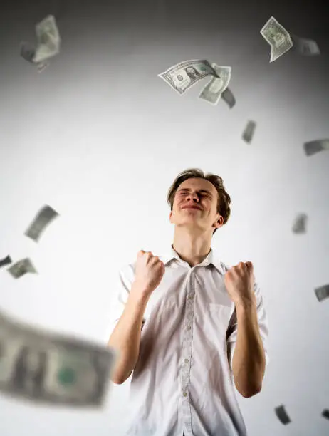 Photo of Young man in white is rejoicing. Success and happiness concept. Man in white and dollars.