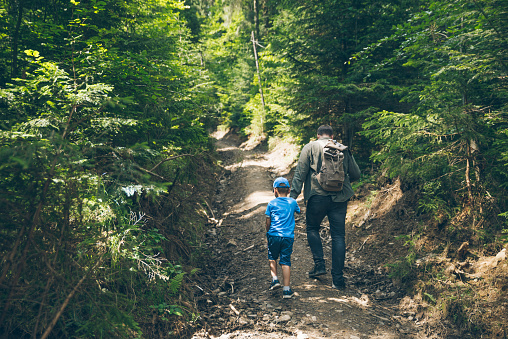 father with little son walking by forest trail. hiking concept