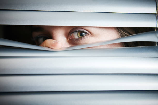 istock Woman's eyes peep through closed white Venetian blind 1138108217