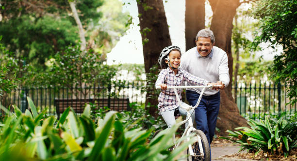 Once you learn, you never forget Shot of an adorable little girl being taught how to ride a bicycle by her grandfather at the park young grandparents stock pictures, royalty-free photos & images