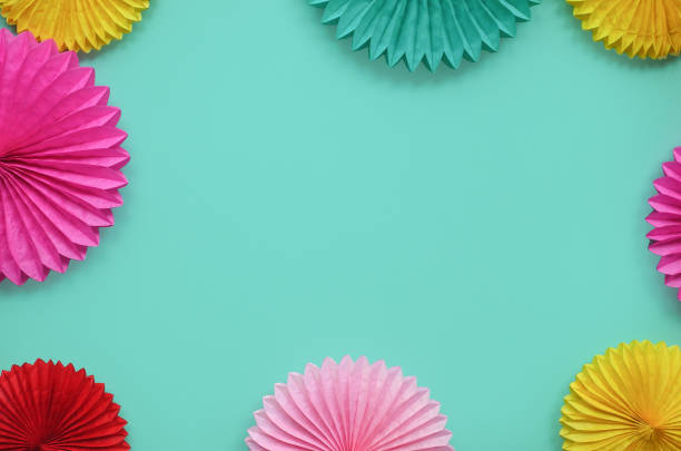 istock Paper flowers on green table top view. Festive or party background. Flat lay style. Copy space for text. Birthday greeting card. 1138112821