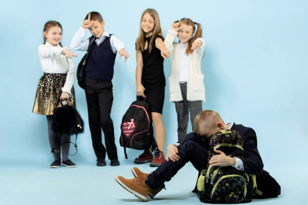 rapaz pequeno que senta-se sozinho no assoalho e que sofre um ato do bullying. - bullying child teasing little boys - fotografias e filmes do acervo